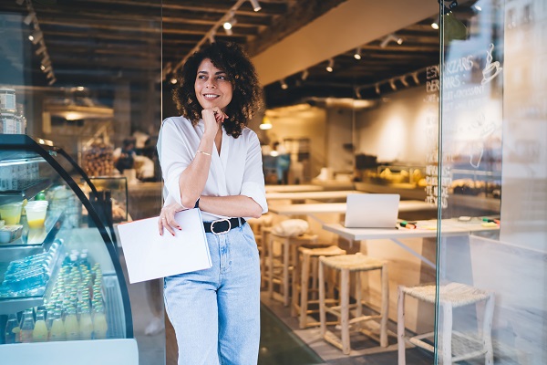 Happy female manager with menu in hand standing in doorway of lo